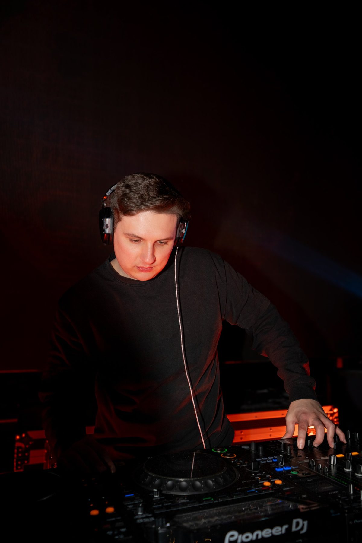 DJ Mike Demero wearing headphones, focused on his Pioneer console under red lighting