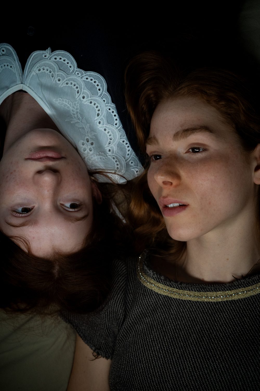 Two red-haired young women lying head to toe against a black background