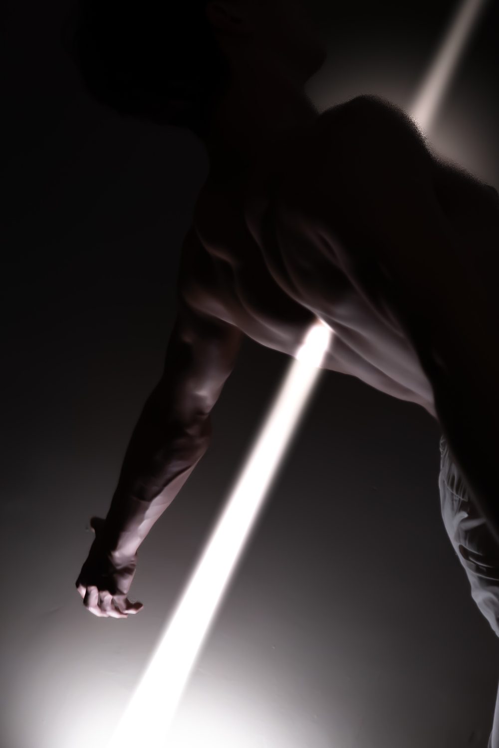A man's torso in near darkness, crossed by a beam of white light